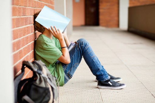 tired male student using book cover his face