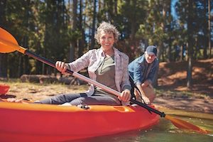 Portrait of happy senior woman in a kayak holding paddles Woman canoeing with man in background at the lake