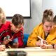 Four children collaborating on a project at a low table, drawing and writing with markers in a bright room,