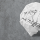 Crumbled white paper shaped like a brain on a grey concrete surface, with algebra formulas sketched on it (e.g., M =, y = mx + b).